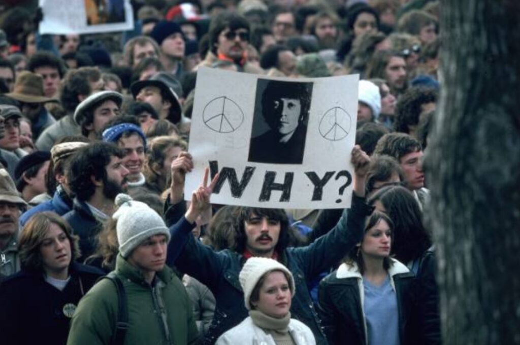 Fans holding a vigil for John Lennon in December 1980, displaying signs with messages of peace and love after his tragic death outside his New York City home.